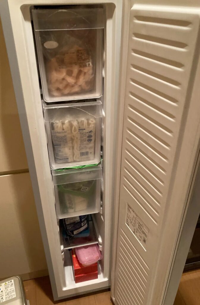 スリム型冷凍庫の中身。引き出しに冷凍うどんや食品を整理して収納している様子