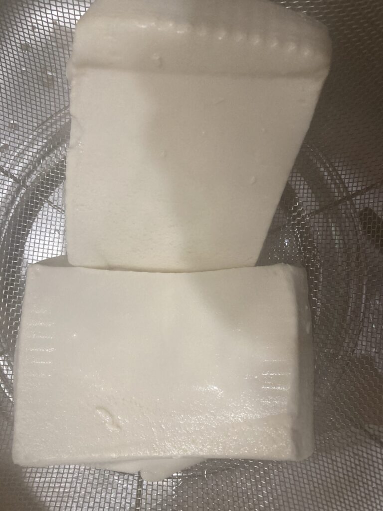 ザルに入れた豆腐を置いて水分を抜いている様子