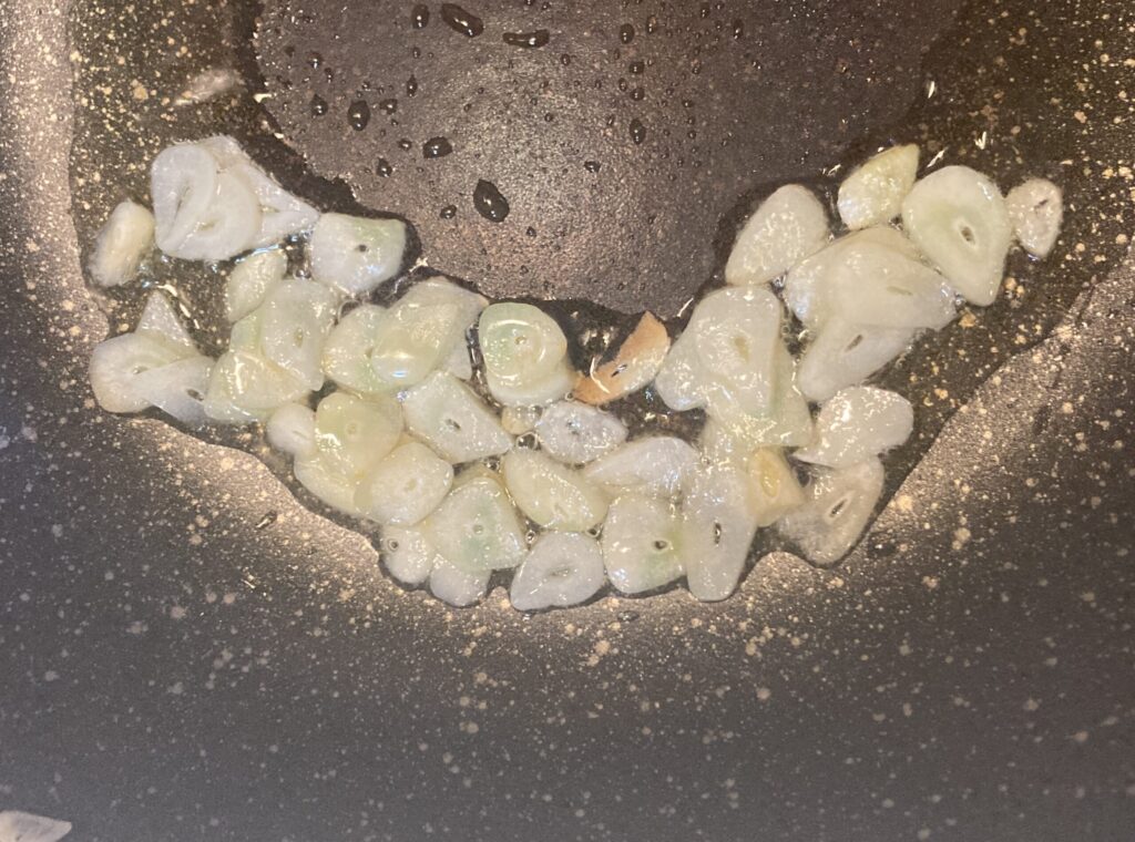 フライパンに油を入れてスライスしたにんにくを炒めている様子。パスタソースの香り付け工程。