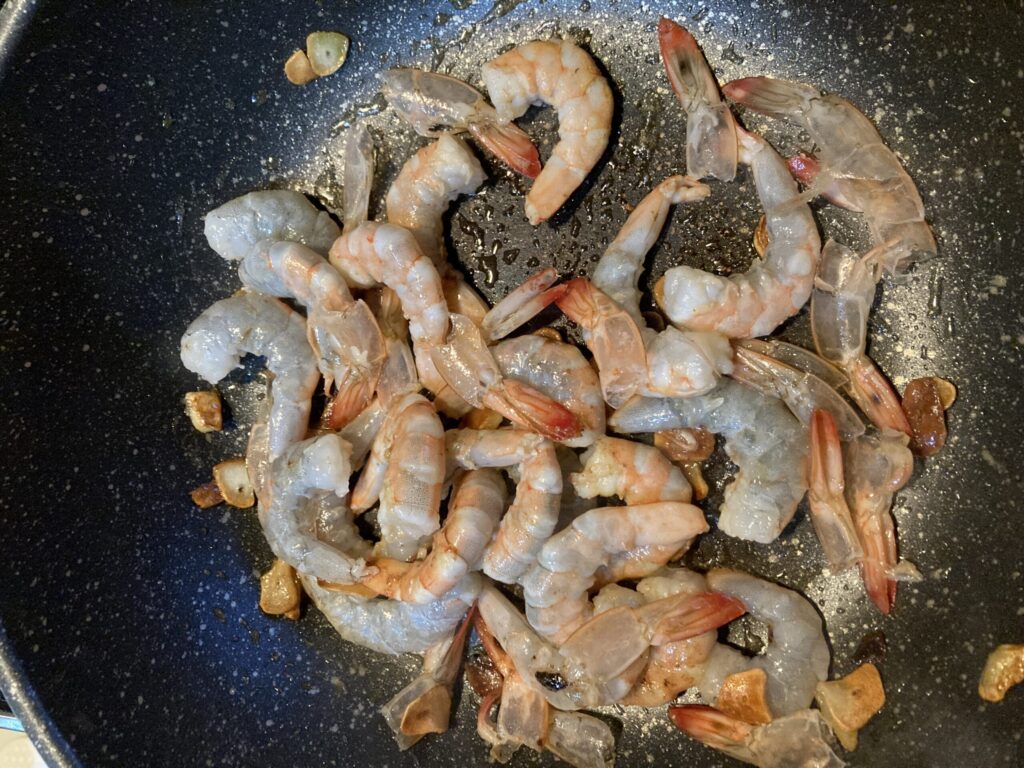 フライパンでにんにくと一緒にエビを炒めている様子。ロゼパスタ用のシーフードを調理している工程。