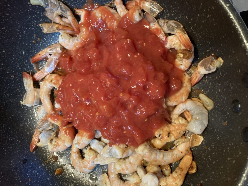 フライパンで炒めたエビにトマト缶を加えてロゼパスタのソースを作っている様子。