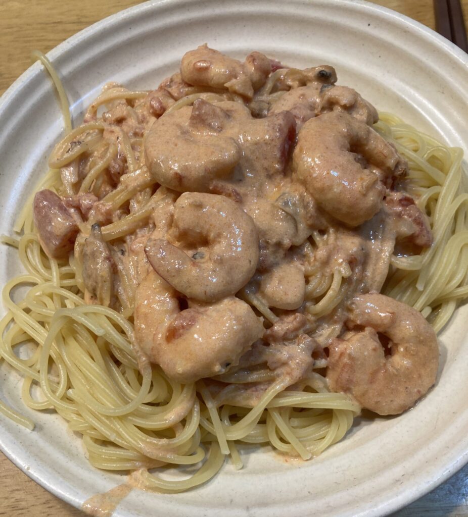 茹でたパスタを皿に盛り、エビとアサリのロゼソースをかけた完成直前の様子。