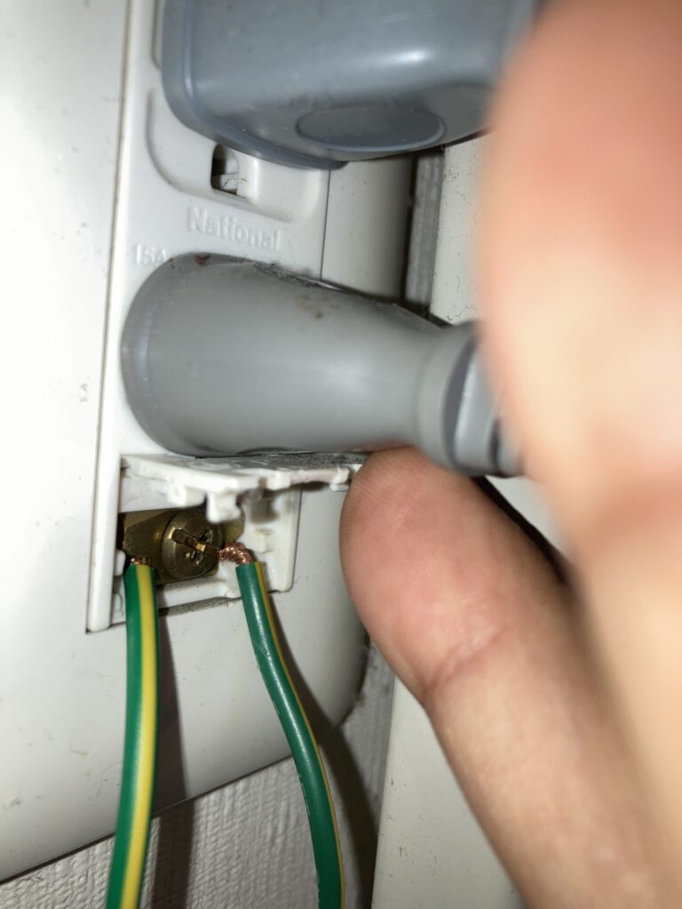 洗濯機のアース線をコンセントから取り外す作業