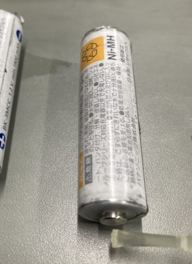 単三充電池のプラス端子に接点復活剤を塗布している写真