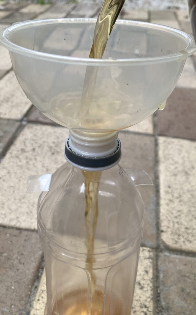 ALT:漏斗を使ってペットボトルに木酢液を少量ゆっくり注ぎ入れている様子の写真