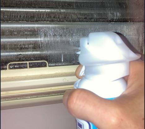 エアコンのアルミフィンに洗浄スプレーを吹き付けて掃除している様子