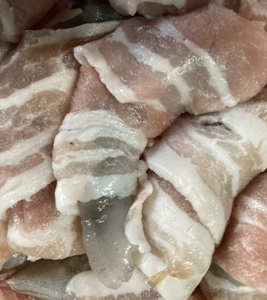 エビに豚バラ薄切り肉を巻きつけている下ごしらえの様子