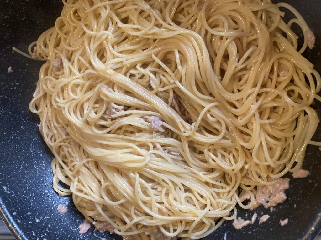 フライパンでツナと調味料を混ぜながらパスタを絡めている様子(ツナ醤油パスタの調理中)
