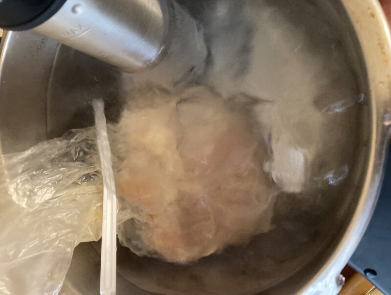 低温調理器を67℃に設定し、袋に入れた鶏むね肉を湯せんする様子(サラダチキン調理中)