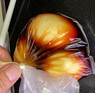 煮卵をビニール袋に入れて、つけ汁につけている写真